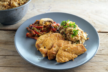 fried chicken filet with cauliflower rice and vegetable ragout of peppers and mushrooms, healthy low carb meal on a blue plate and a rustic wooden table, selected focus, narrow depth of field