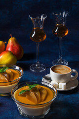 Panna cotta Italian traditional dessert with pears poached in rum and honey syrup. Dark blue background table, glasses of rum, jar of honey, pears and spice.