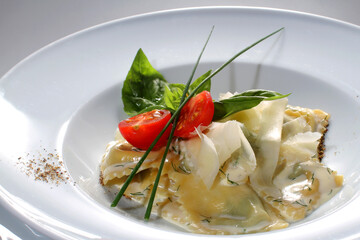 Ravioli with parmesan cheese, herbs and cherry tomatoes on a white plate. Italian ravioli tortellini