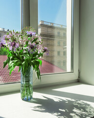 Romance. Wildflowers stand in a vase on a white windowsill. Outside the window is the city.