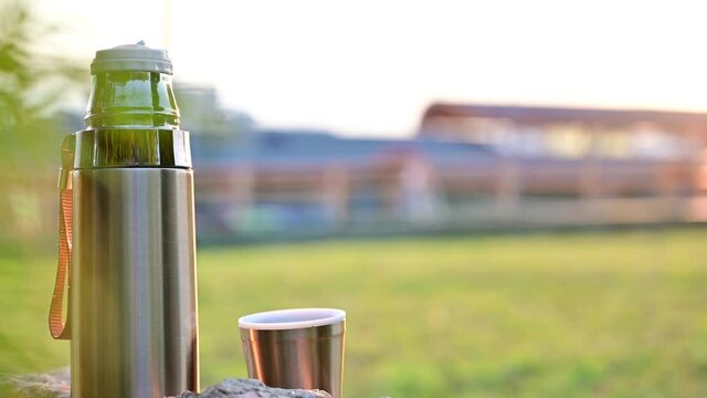Video of a thermos in the evening sun on a background of a landscape without people. Shot in summer in clear weather. Tourist vacation concept.