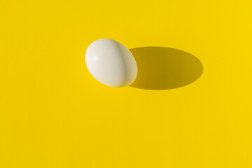 White boiled egg photographed with a hard shadow on a yellow background.