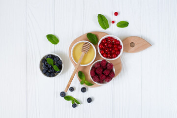 Ingredients for healthy breakfast - fresh rastberry, red currant, blueberry and honey top view on white wooden table. Organic summer food for immunity booster concept