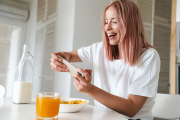 Photo of woman playing online game on cellphone while having breakfast