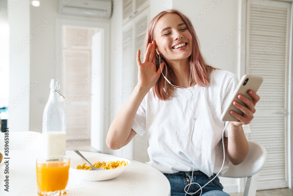 Canvas Prints Photo of woman using cellphone and earphones while having breakfast