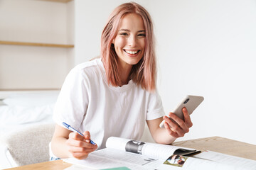 Image of woman using smartphone while doing homework with exercise books