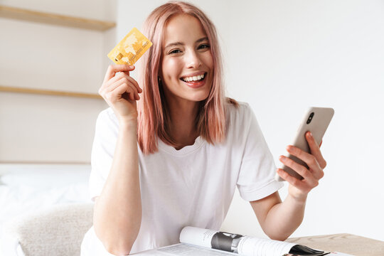 Image of woman holding smartphone and credit card while doing homework