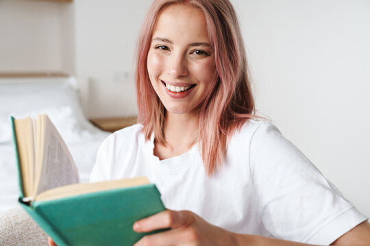 Image of joyful pretty woman reading book and smiling