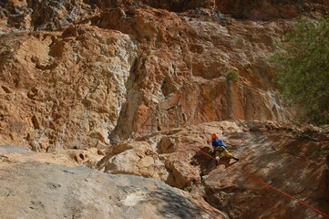 little boy climbs on the rock with rope