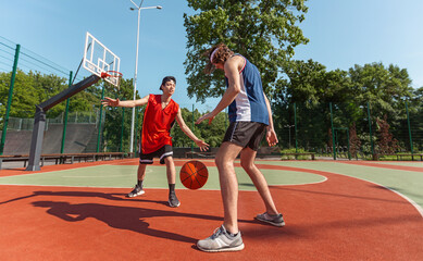 Two millennial sportsmen playing basketball match at outdoor playground