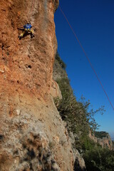 little boy climbs on the rock with rope