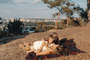 A beautiful young woman lying on blanket with her daughters. Happy family spends their day in the nature. Three blonde females, mother with her two little kids.