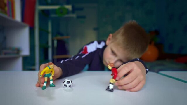Sad boy playing figures of football players. The boy dreams of playing soccer with friends. An upset child in his room near the window The boy dreams of becoming a great football player.