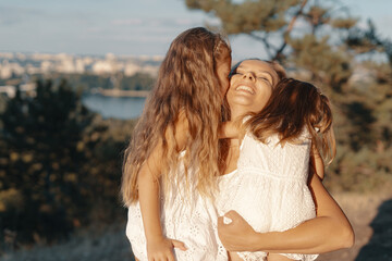 Fototapeta premium A beautiful young woman playing with her daughter. happy family spends their day in the nature. Three blonde females, mother with her two little kids.