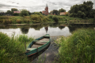 Rural landscape with a river, an old boat and a church