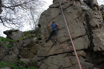 little boy climbs on the rock with rope