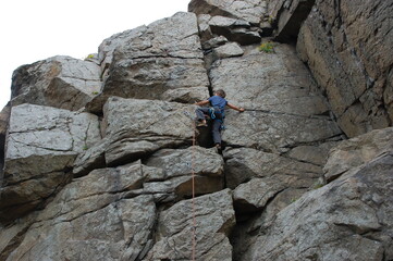 little boy climbs on the rock with rope