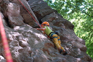 little boy climbs on the rock with rope