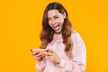 Image of cute pleased woman winking and playing video game on cellphone