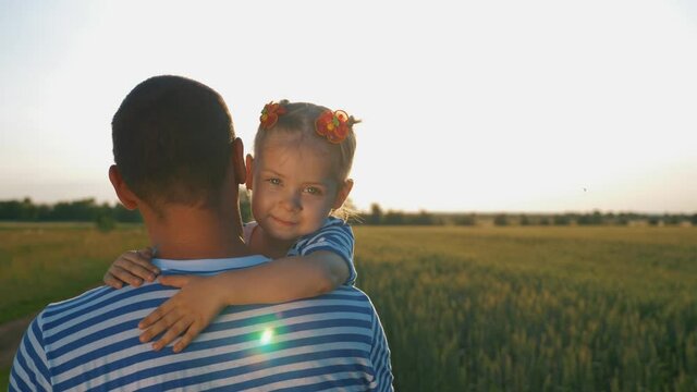 Happy family. A young father holds a child in his arms. Father and daughter hug each other in the open air in the rays of the setting summer sun.