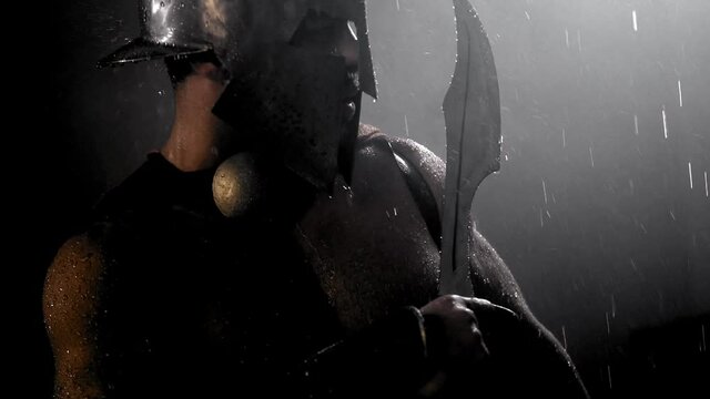 Muscular spartan looking at raindrops on blade.