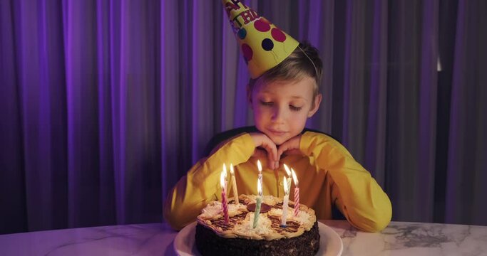 Cute boy blows out candles on a cake on his birthday.  Happy child looks at a cake with candles. Child looks at the cake and makes a birthday wish. Boy celebrates his birthday. Happiness concept