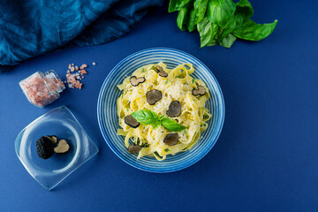 Fettuccine pasta with black truffle and parmesan in a stylish blue bowl on a blue background...