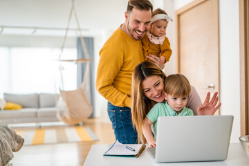 Happy family at home using computer, waving while in a live video chat