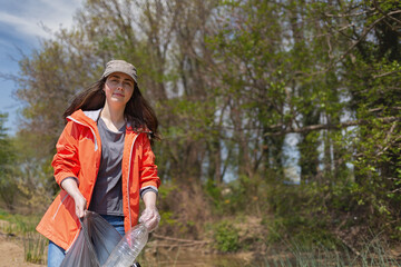 Fototapeta na wymiar A female volunteer smiles and collects garbage in the Park area. The concept of the protection of the environment and Earth Day