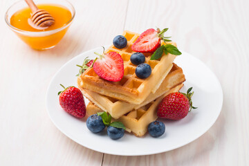 Fresh homemade food of berry Belgian waffles with honey, chocolate, strawberry, blueberry, maple syrup and cream. Healthy dessert breakfast concept with juice