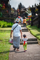 Father and son hold hands and walk together along the path to the temple. Indonesian culture. island of Bali