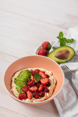 Summer salad with strawberries, avacado and cream cheese on a white wooden background.