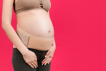 Cropped image of pregnancy belt dressed on pregnant woman for reducing pain in the back at pink background with copy space. Orthopedic abdominal support belt concept