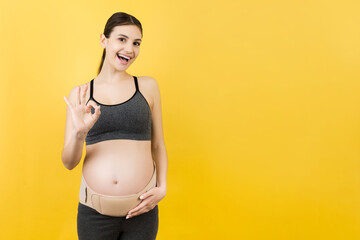 Portrait of pregnant woman on the third trimester wearing pregnancy belt and showing okay sign at...