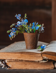 Mini bouquet of wild flowers in a decorative bucket on old books on the village window.