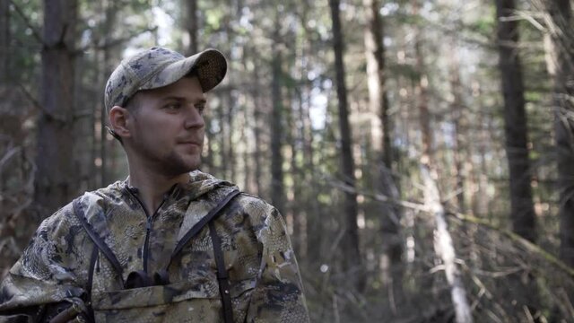 Portrait of handsome young man hunter or tourist. Man in camouflage clothes hunts outdoor in forest hunting alone. Close up of man hiker standing in forest. Hunter searching animal tracks.