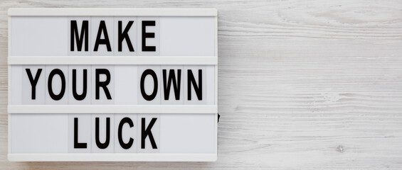 'Make your own luck' on a lightbox on a white wooden background, top view. Flat lay, from above, overhead. Copy space.