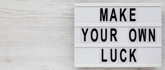 'Make your own luck' on a lightbox on a white wooden surface, top view. Flat lay, from above, overhead. Copy space.