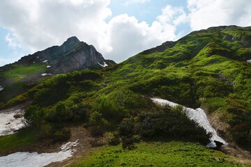 Alpine landscape. White clouds over high rocky mountains. Snow lies on the slopes of the mountains....