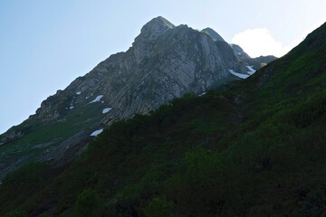 Alpine landscape. White clouds over high rocky mountains. Snow lies on the slopes of the mountains. Spring morning over the Alps.