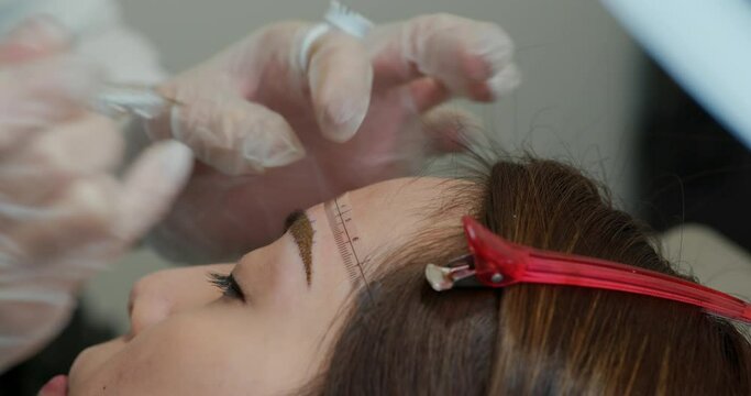 Cosmetologist applying permanent make up on woman eyebrow