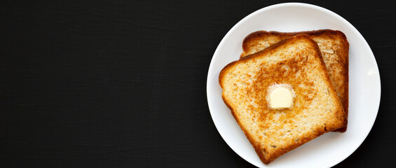 Homemade Buttered Toast on a white plate on a black surface, top view. Flat lay, overhead, from above. Copy space.