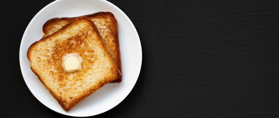 Homemade Buttered Toast on a white plate on a black background, top view. Flat lay, overhead, from above. Copy space.