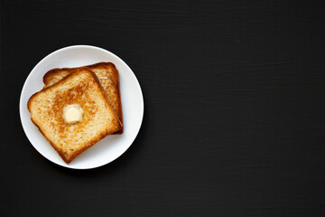 Homemade Buttered Toast on a white plate on a black surface, top view. Flat lay, overhead, from above. Copy space.