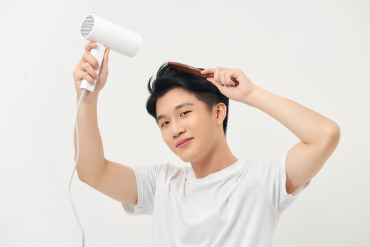 Handsome young man drying his hair and smiling while standing against white background