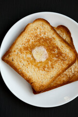Homemade Buttered Toast on a white plate on a black background, top view. Flat lay, overhead, from above.