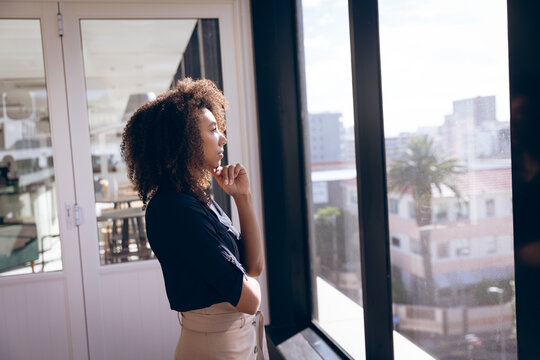 Young mixed race businesswoman thinking in front of windows