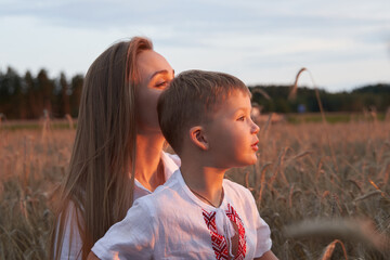Obraz premium Portrait of cheerful son with camera sitting on mothers laps amidst wheat field