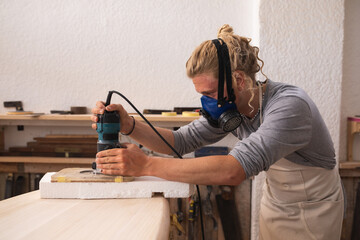 Caucasian male surfboard maker wearing a face mask working in his studio making a surfboard