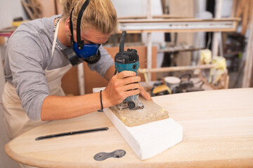 Caucasian male surfboard maker wearing a face mask working in his studio making a surfboard